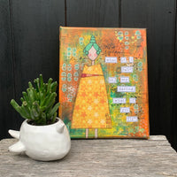 Original mixed-media canvas beside a plant. The canvas is painted in vivid colour of green and orange with a faceless lady in a bright yellow & orange dress of stars with green hair. The quote reads, "What if I fall? Oh my darling, what if you fly?