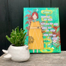 Load image into Gallery viewer, mixed-media collage of girl in patterned yellow dress with turquoise green, yellow &amp; red background. words are cut out and pasted on stating, &quot;attract what you expect, reflect what you desire, become what you respect, mirror what you admire&quot;. Black background canvas sits on wood surface beside a plant for scale.
